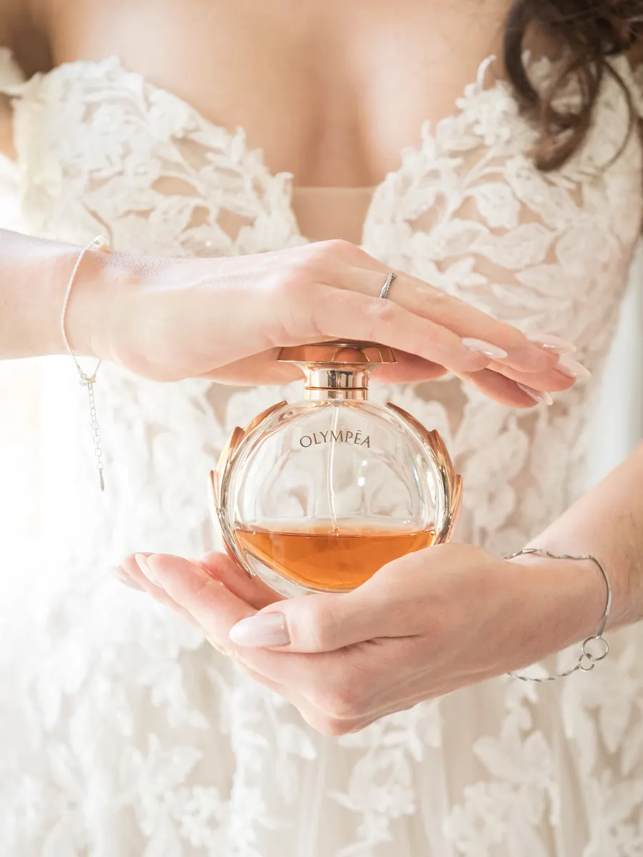 Braut hält ihr Parfum vor dem Spitzenkleid – Hochzeit Celina & Sebastian in Rodgau