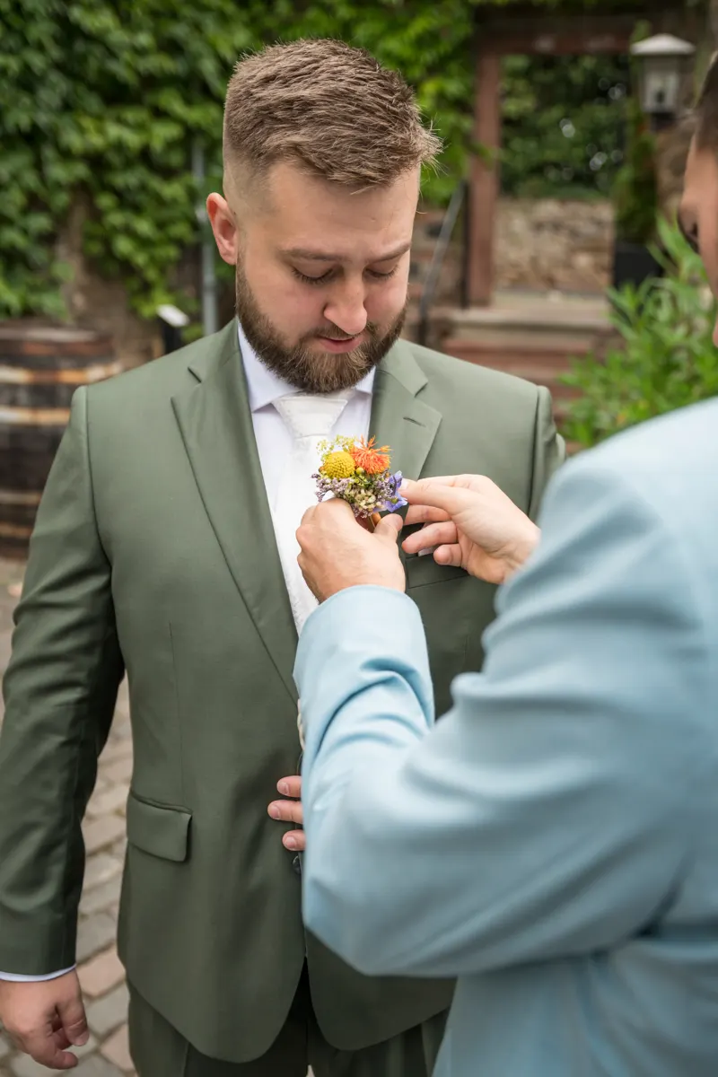 Trauzeuge steckt dem Bräutigam den Anstecker an – Hochzeit Vanessa & Dennis